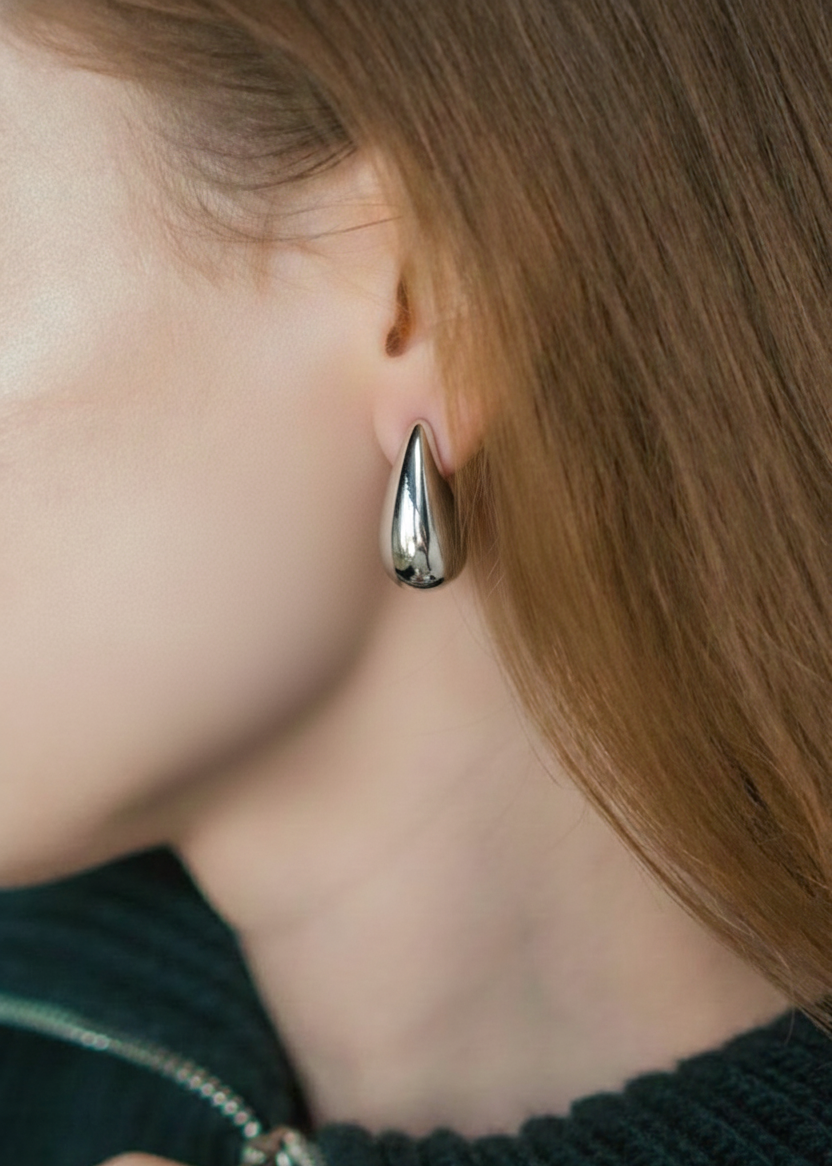 Close-up of a woman's ear wearing a shiny silver teardrop-shaped earring with brown hair