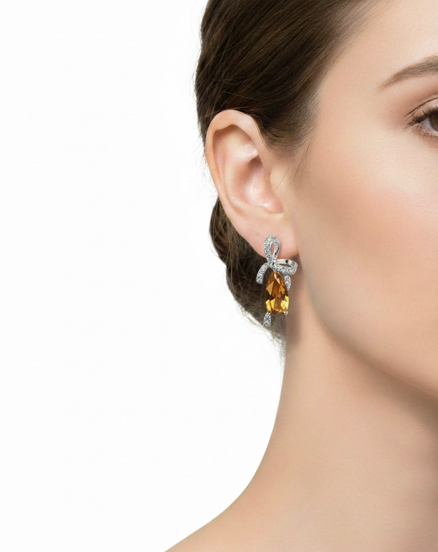 Close-up of a woman's ear wearing elegant silver earrings with amber-colored gemstones and diamond accents