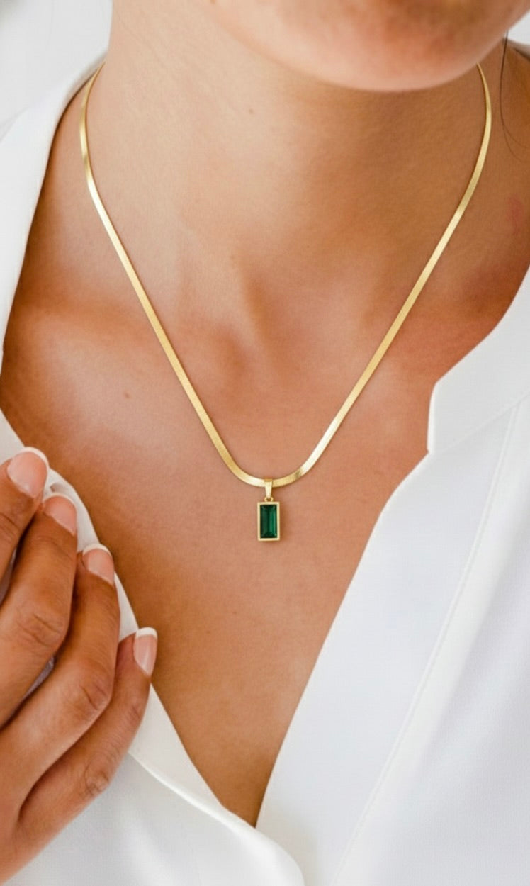Close-up of woman wearing gold necklace with rectangular green gemstone pendant and white shirt